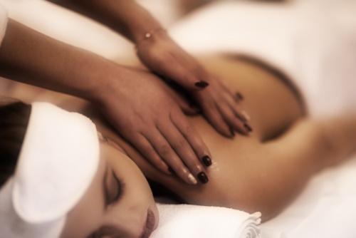 Close up image of a young woman who laying on her stomach and receiving a back massage